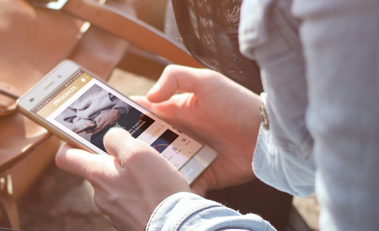 A person holding a smartphone with the open ERDINGER Fan App displayed on the screen.