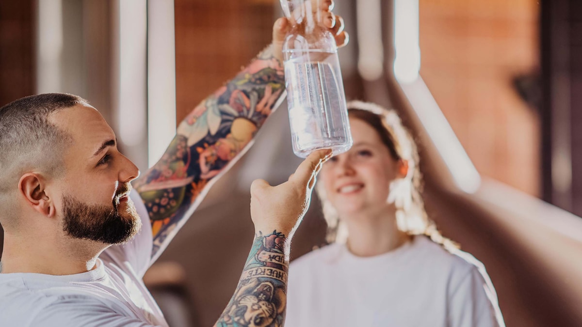 Two ERDINGER brewers examine a water sample in a glass.