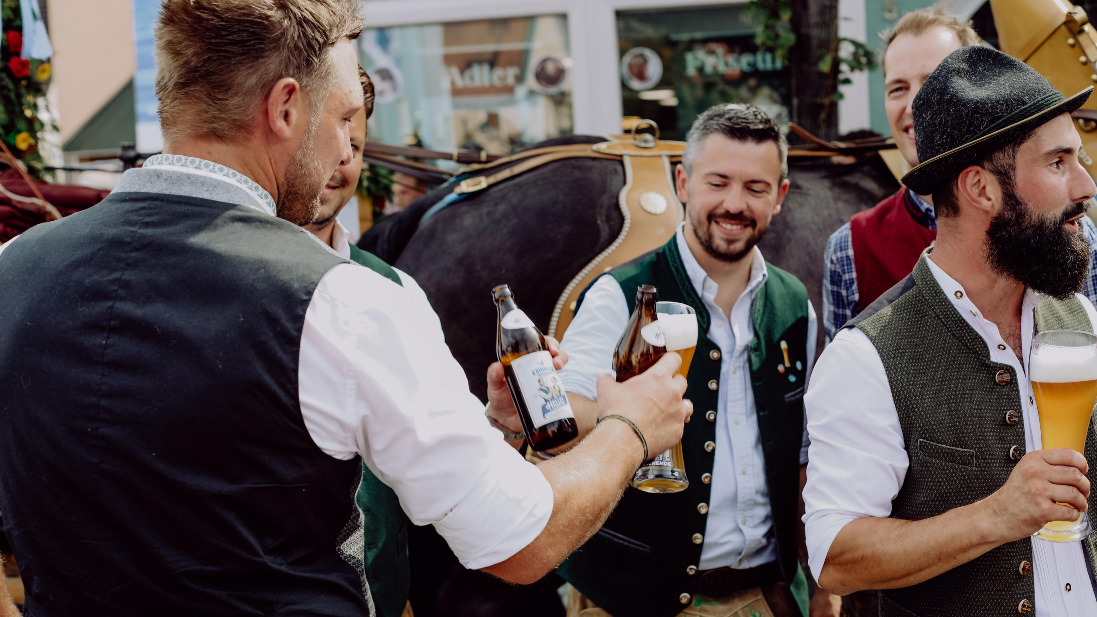 Mehrere ERDINGER Mitarbeiter in Tracht prosten sich zu bei einem Festumzug der Brauerei.