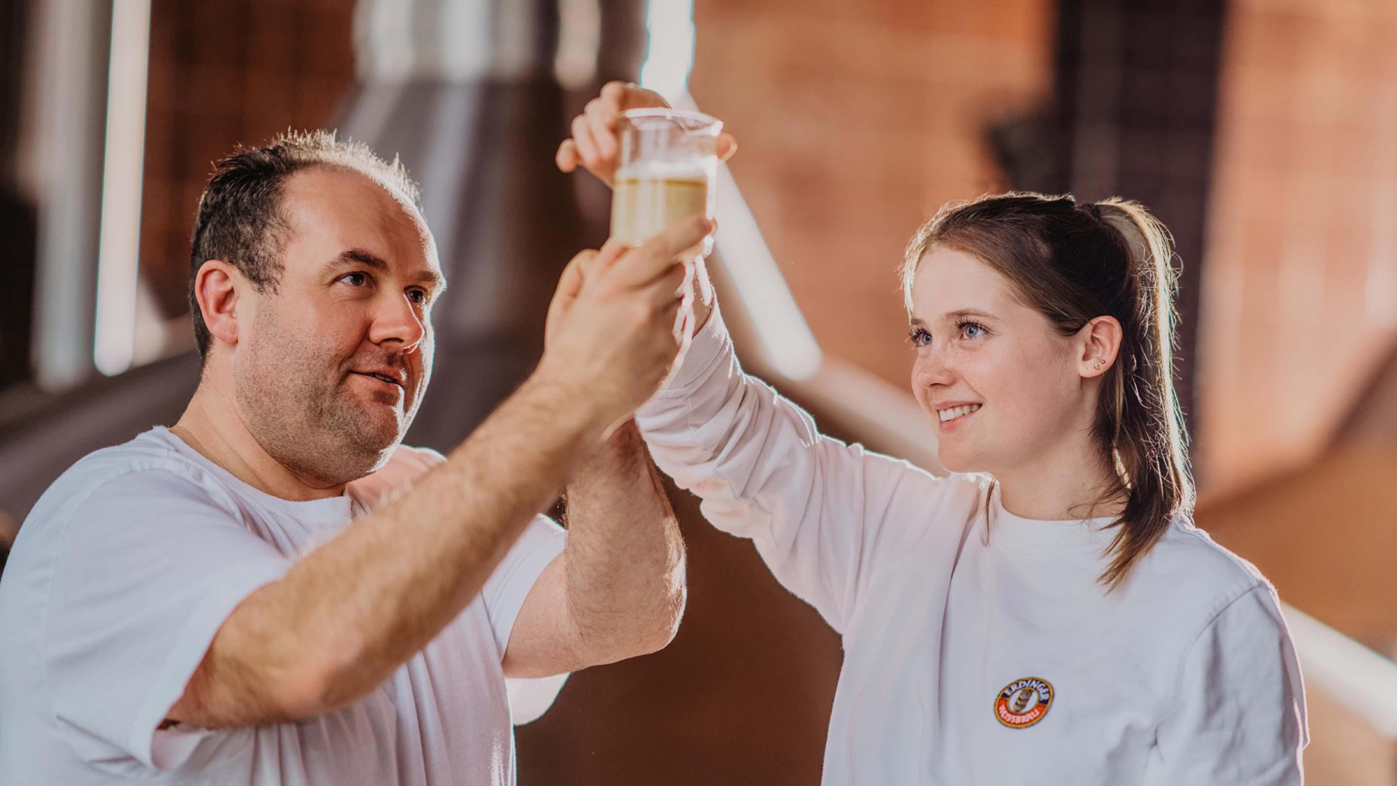 Zwei ERDINGER Brauer prüfen Hopfenpallets, die Brauerin hält den Hopfen in den Händen und riecht daran.