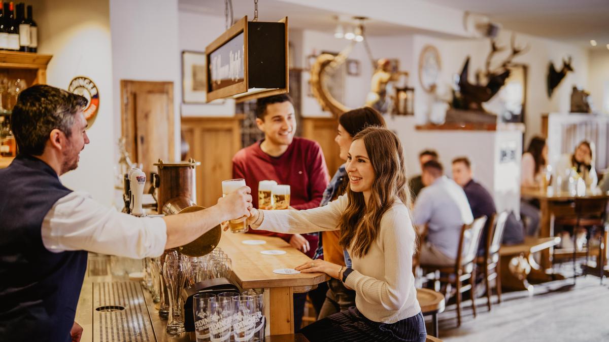 Ein ERDINGER Mitarbeiter reicht einer lächelnden Frau ein Bier über die Schanktheke im Besucherzentrum der Brauerei.