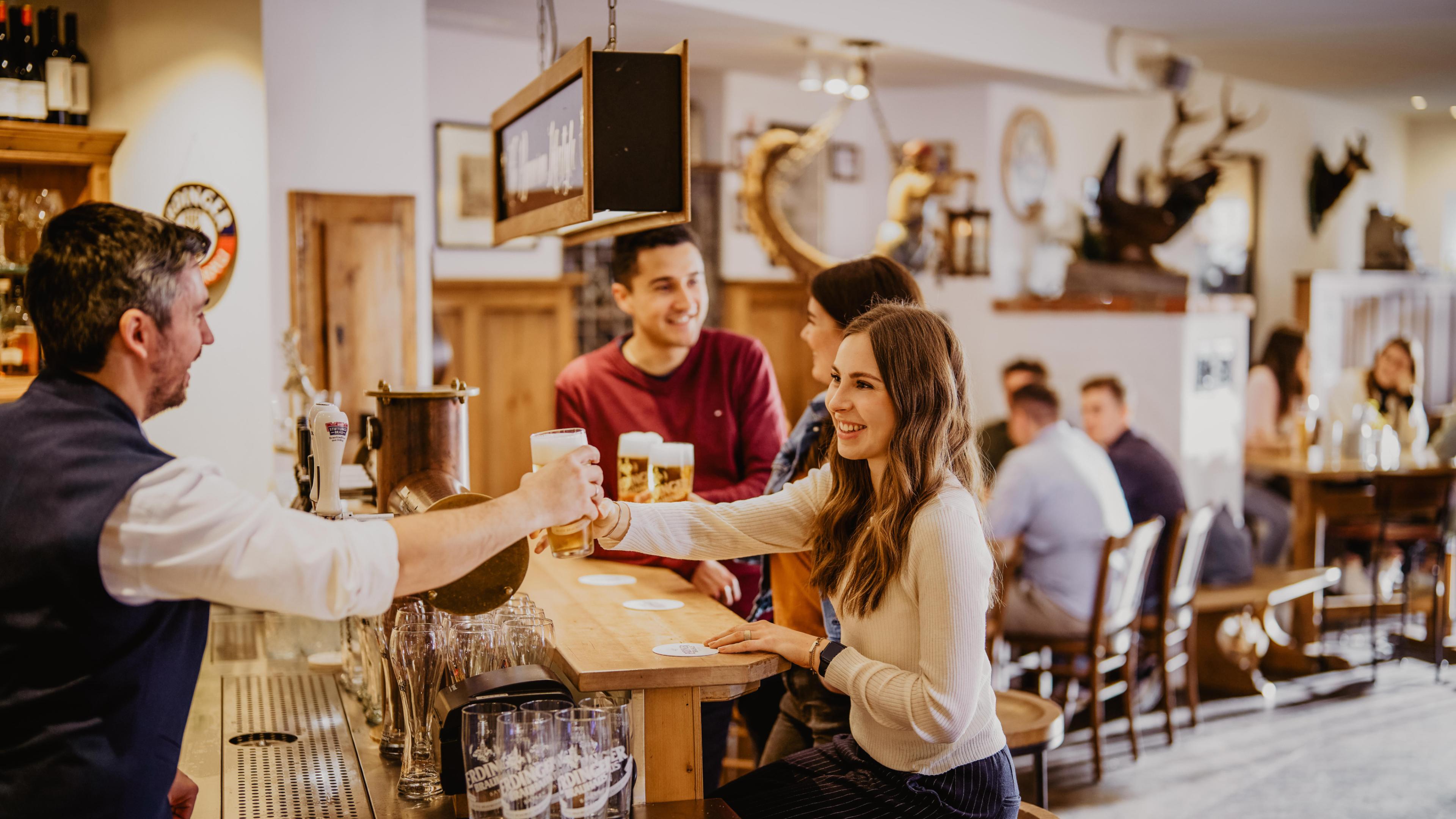 Ein ERDINGER Mitarbeiter reicht einer lächelnden Frau ein Bier über die Schanktheke im Besucherzentrum der Brauerei.