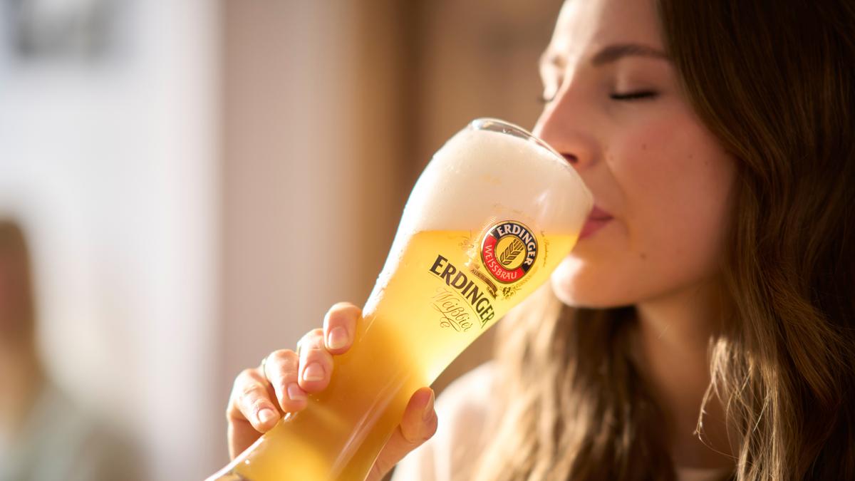 Eine Frau nimmt einen genüsslichen Schluck von einem frisch gezapften ERDINGER Weißbier.