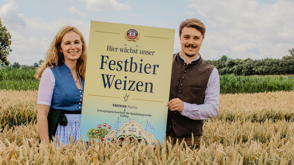 Alexandra Graf von ERDINGER und Daniel Gschlößl von der EZG posieren zusammen mit Festbier-Weizen-Schild vor regionalem Weizen.