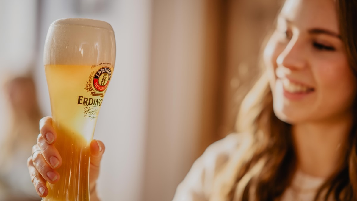 Eine Frau hält ERDINGER Weißbier in einem Glas gegen das Licht.