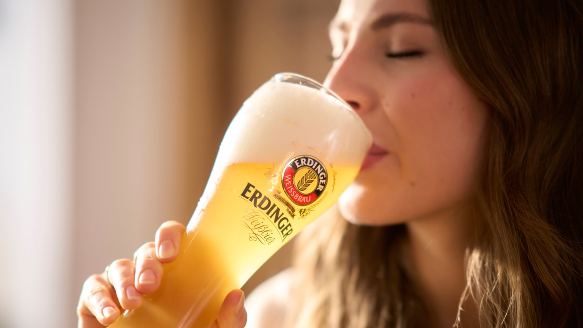 Eine Frau nimmt einen genüsslichen Schluck ERDINGER Weißbier im Glas.