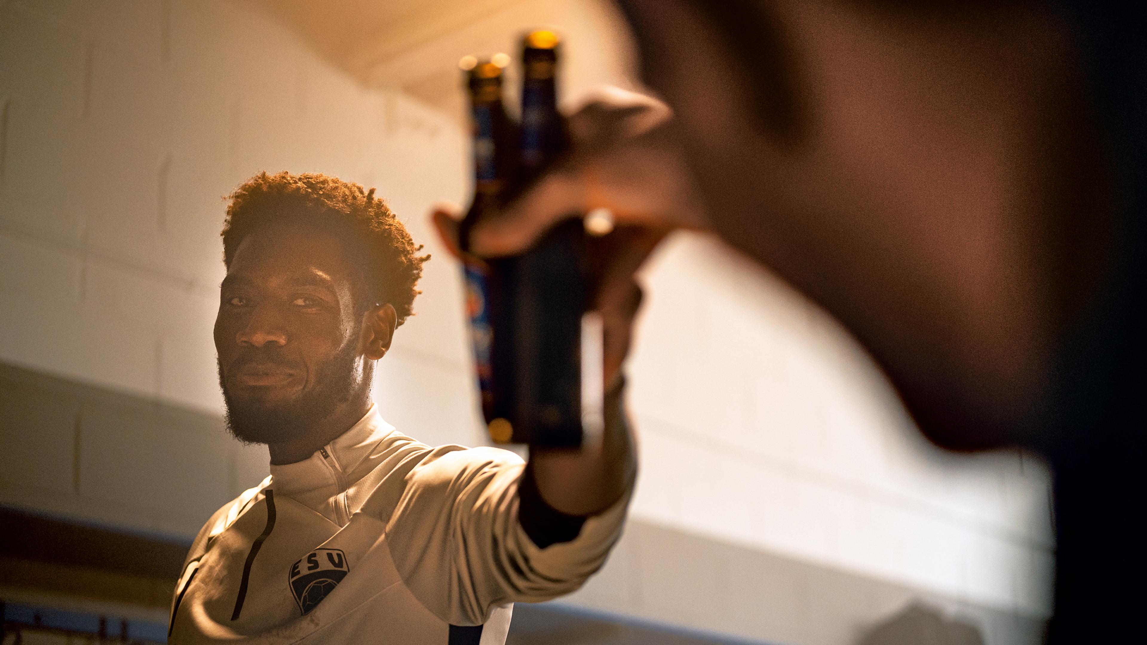 Zwei Männer prosten sich in einer Kabine nach dem Training mit ERDINGER Alkoholfrei zu.