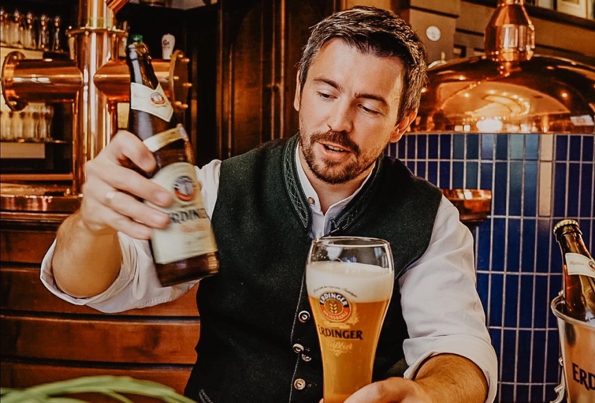 Ein Barkeeper schüttet die Hefe aus der Flasche auf die Schaumkrone vom ERDINGER Weißbier.