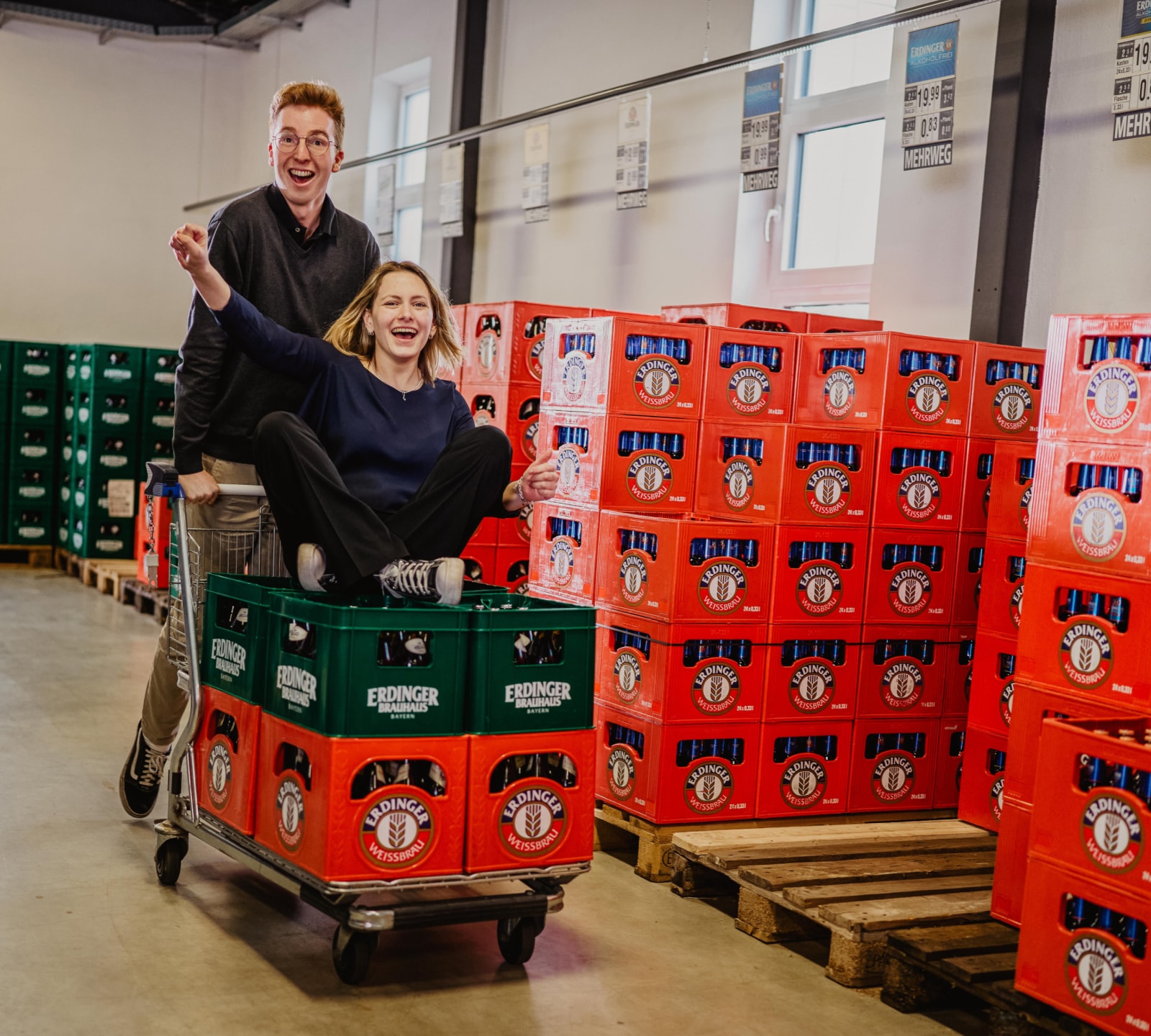 Fröhliche Auszubildende mit Einkaufswagen und Bierkisten in ERDINGER Haustrunkausgabe.