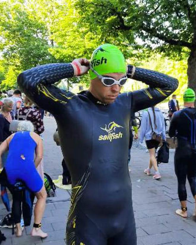 Ein Mann im Neoprenanzug und mit Schwimmhaube zieht eine Schwimmbrille an.