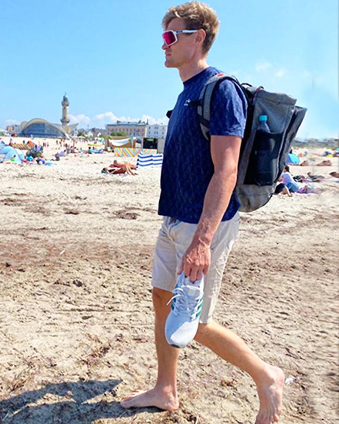 Ein Mann mit einem Rucksack läuft über einen Strand