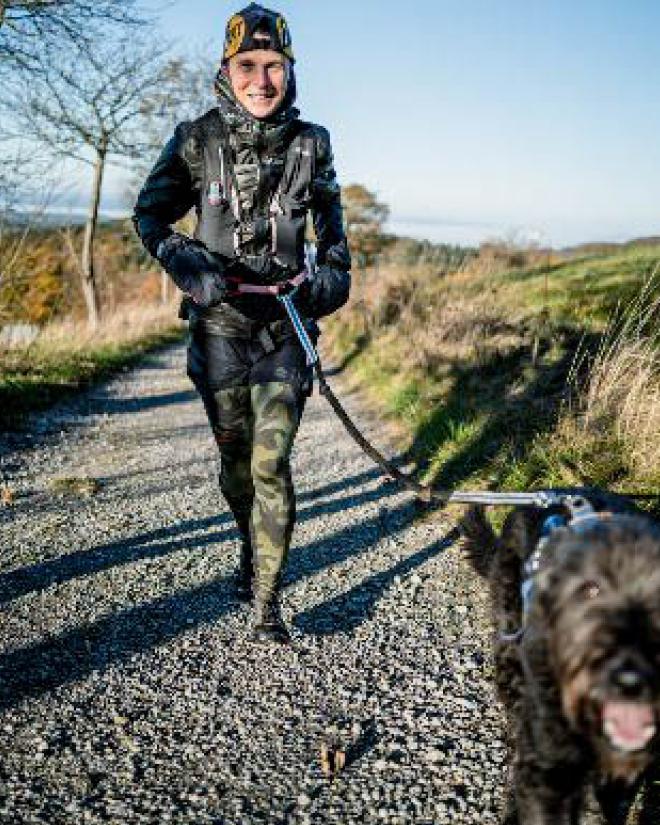 Eine lächelnde Frau spaziert mit ihrem Hund in der Natur.