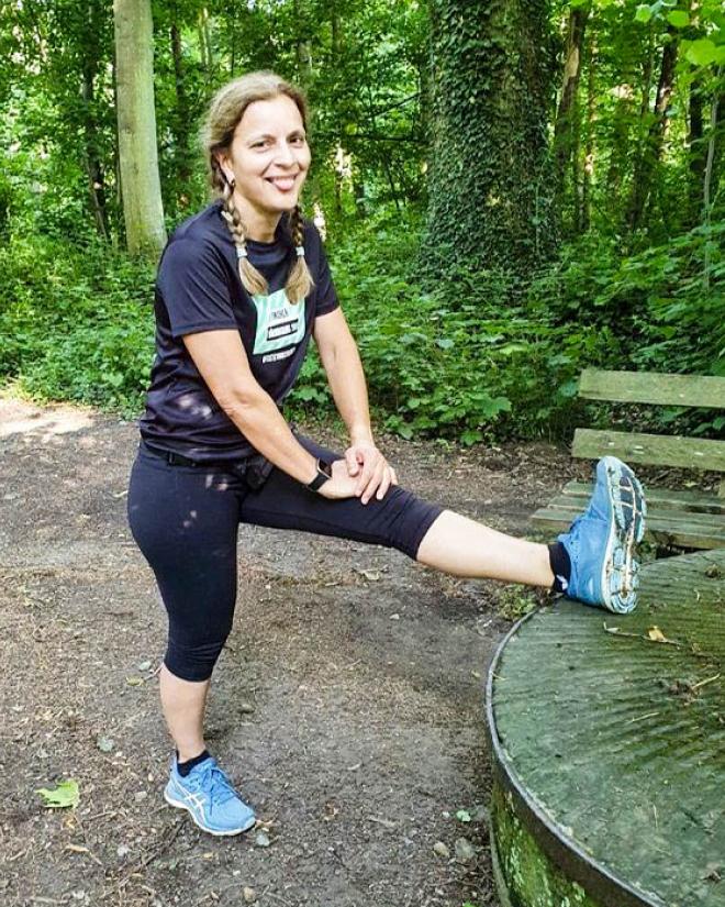 Eine Frau dehnt sich vor dem Lauf in der Natur an einem alten moosbewachsenen Mühlstein.