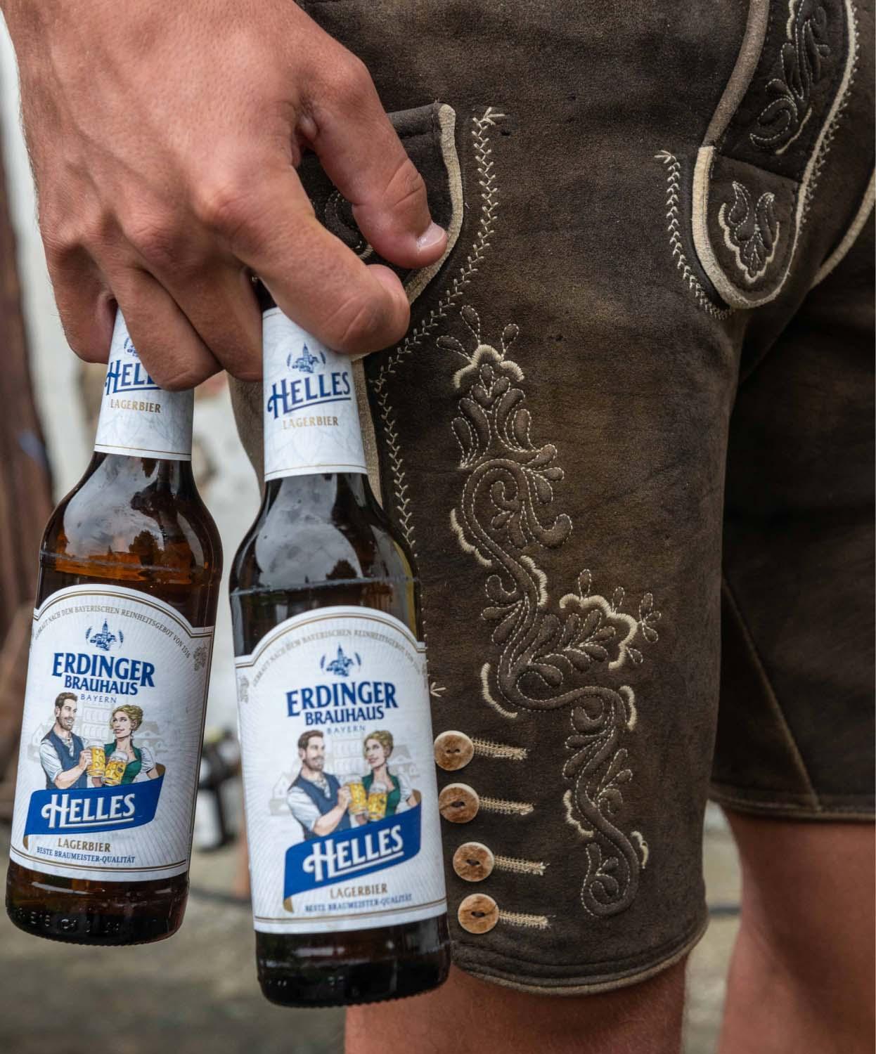 Ein Mann hält zwei Flaschen ERDINGER Brauhaus Helles vor seiner Lederhose.